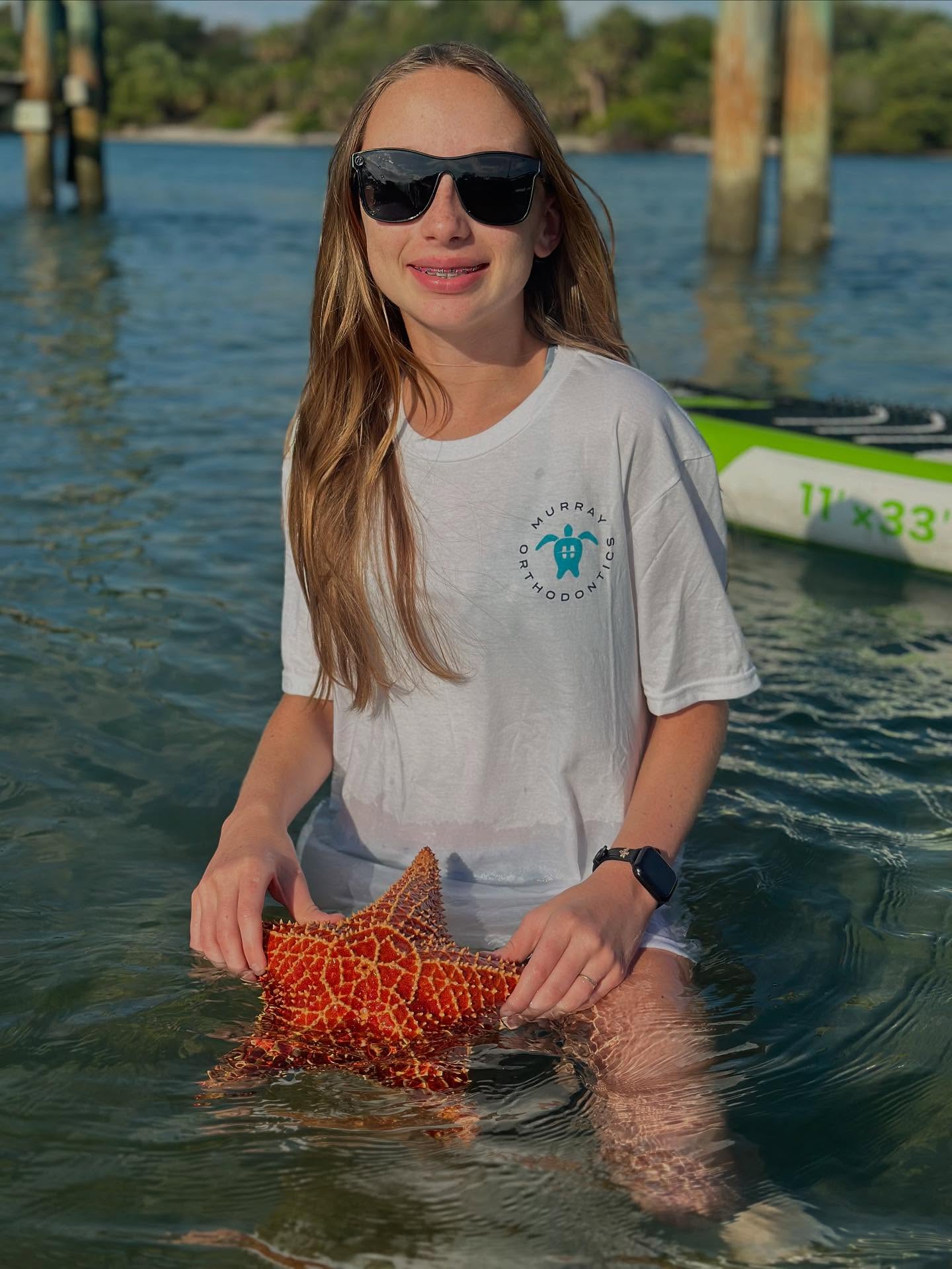 Murray Orthodontics patient with braces wearing branded shirt and holding a starfish in South Florida