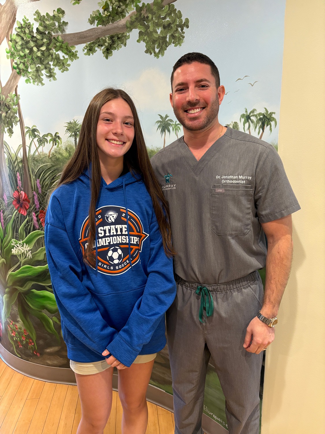 Dr. Jonathan Murray with a teenage patient wearing a state soccer championship hoodie at Murray Orthodontics Royal Palm Beach