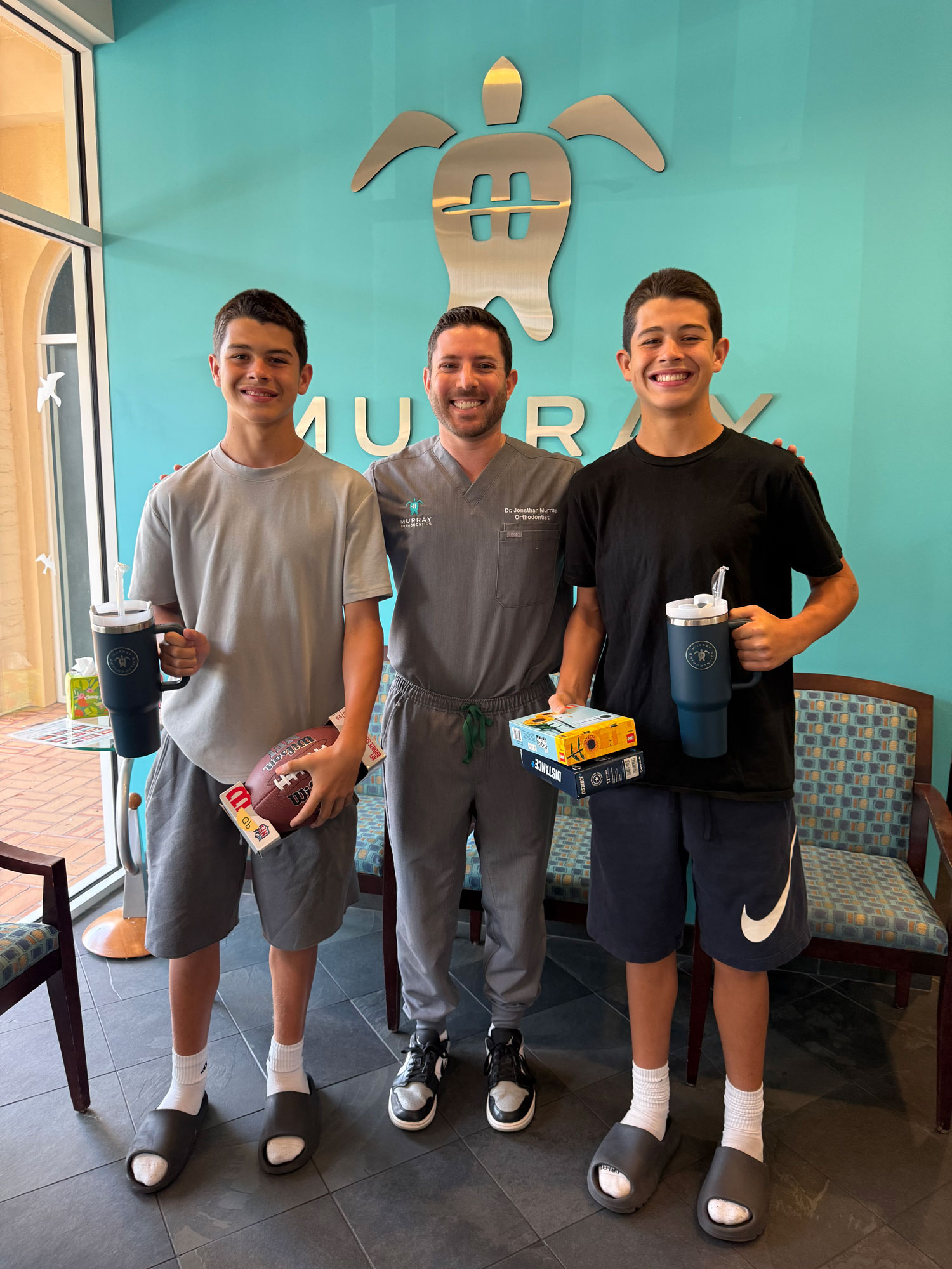 Dr. Jonathan Murray with two teen orthodontic patients holding prizes in the Palm Beach Gardens Murray Orthodontics waiting room