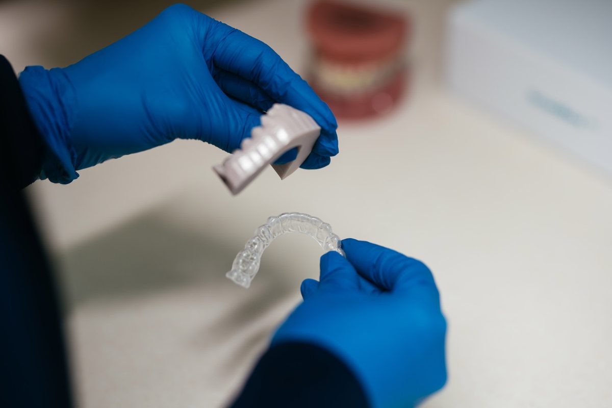 Blue-gloved orthodontic team member holding a clear Invisalign aligner tray and attachment template at Murray Orthodontics in Palm Beach Gardens
