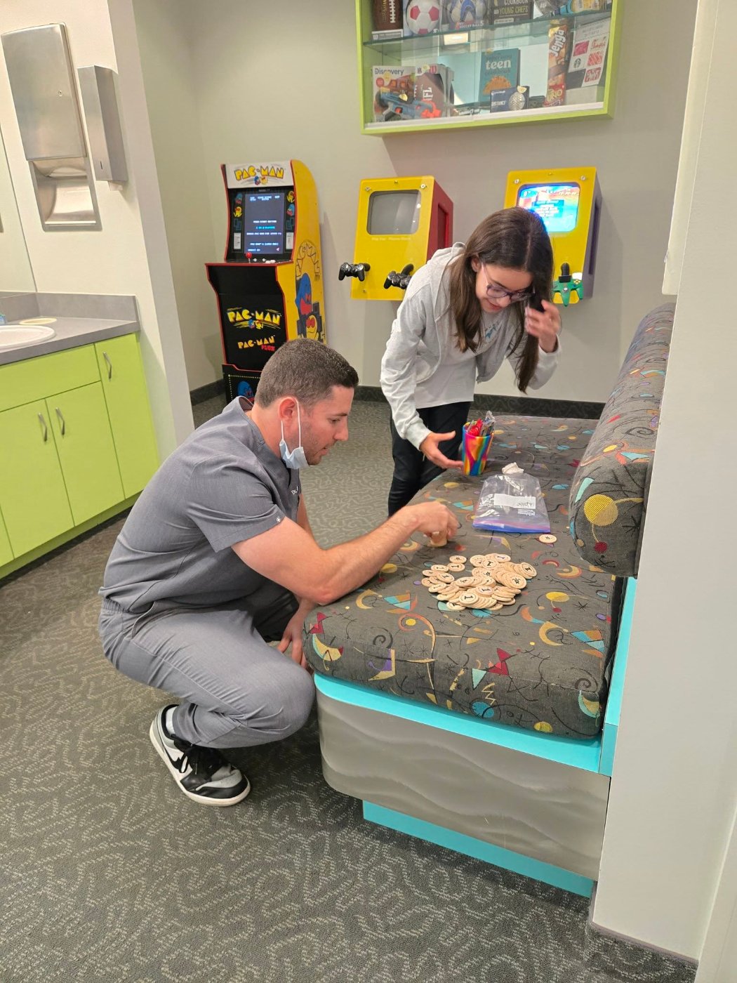 Dr. Jonathan Murray counting prize tokens with a young patient in the game room at Murray Orthodontics in Palm Beach Gardens, FL