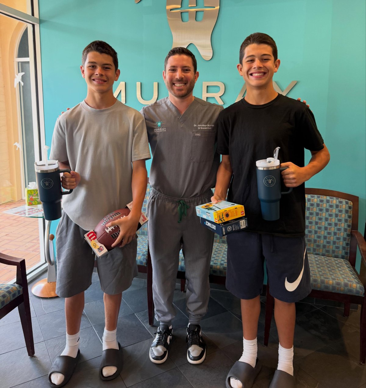 Dr. Jonathan Murray with twin teen patients holding prizes on the day they finished treatment at Murray Orthodontics